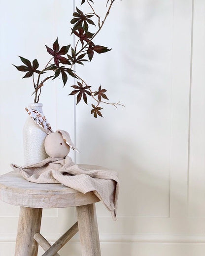 Decorative setup with a vase, plant, and small figurine on a wooden stool against a white paneled wall.